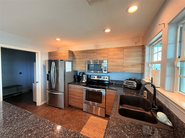 kitchen featuring dark stone countertops, recessed lighting, a sink, appliances with stainless steel finishes, and brown cabinets