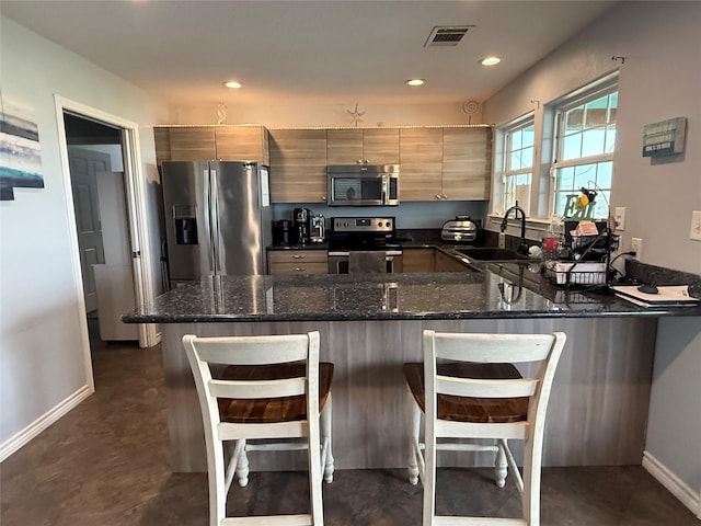 kitchen featuring visible vents, dark stone countertops, a peninsula, stainless steel appliances, and a sink