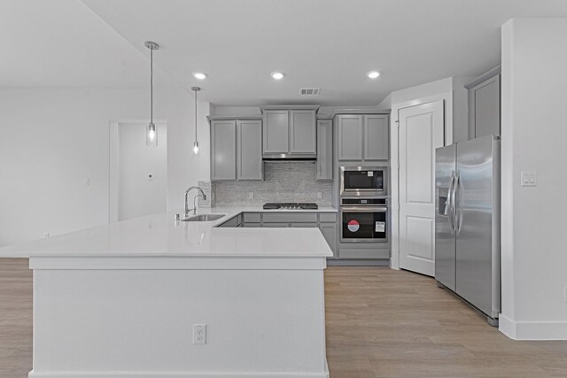 kitchen with a peninsula, gray cabinetry, a sink, light countertops, and appliances with stainless steel finishes