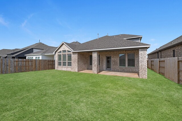 back of house with brick siding, a shingled roof, a lawn, a fenced backyard, and a patio area