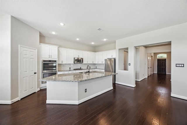 kitchen with light stone counters, appliances with stainless steel finishes, white cabinetry, and dark wood-type flooring