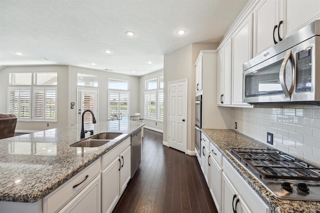 kitchen with dark wood finished floors, a sink, decorative backsplash, stainless steel appliances, and white cabinets