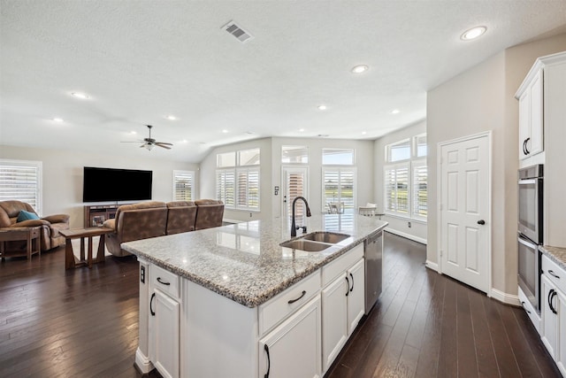 kitchen featuring dark wood finished floors, open floor plan, an island with sink, stainless steel appliances, and a sink