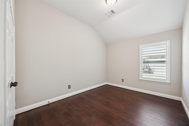 spare room featuring dark wood-style floors, visible vents, baseboards, and lofted ceiling