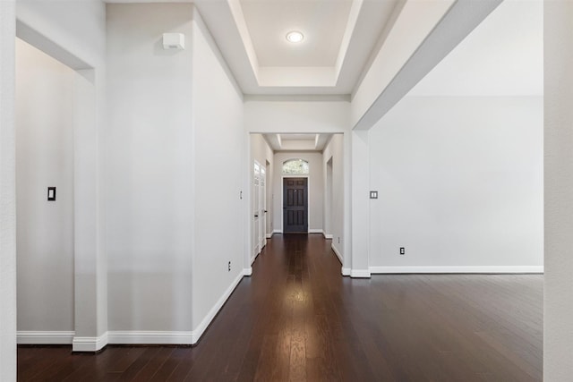 hall with dark wood-style floors, a raised ceiling, and baseboards