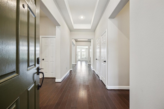 hallway with baseboards, dark wood-type flooring, and a raised ceiling