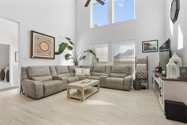 living area with a ceiling fan, light wood-style flooring, separate washer and dryer, and a towering ceiling