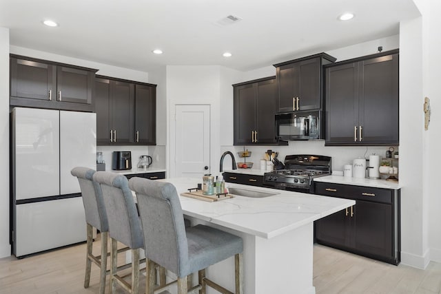 kitchen featuring visible vents, a sink, freestanding refrigerator, range with gas cooktop, and black microwave