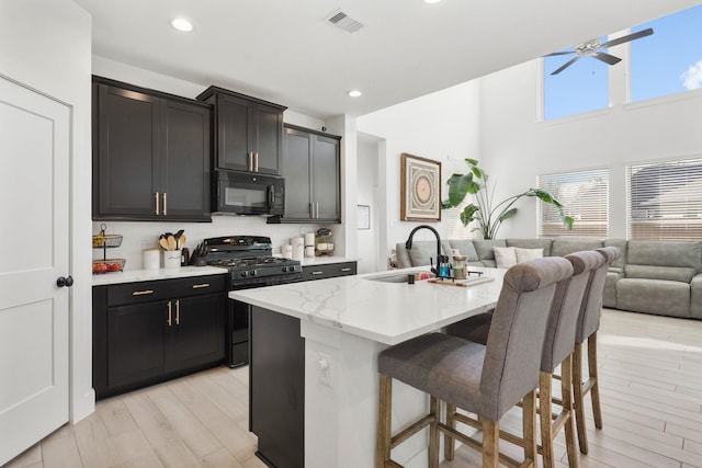 kitchen featuring visible vents, black appliances, a breakfast bar, a sink, and open floor plan