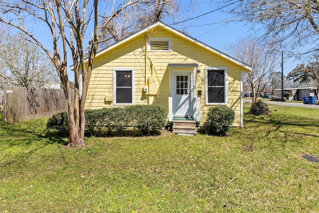 bungalow-style home with entry steps, a front lawn, and fence