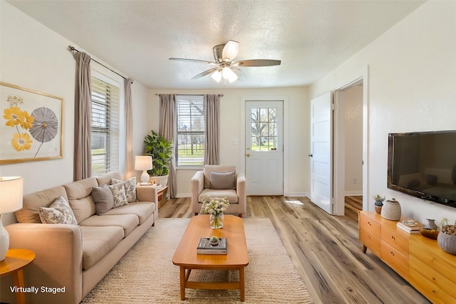 living area with baseboards, a textured ceiling, light wood-style flooring, and a ceiling fan