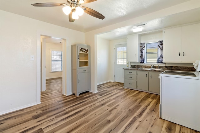 kitchen featuring a sink, dark countertops, white cabinetry, light wood-style floors, and stove