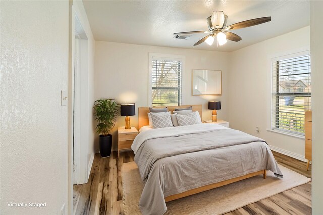 bedroom with ceiling fan, visible vents, multiple windows, and wood finished floors