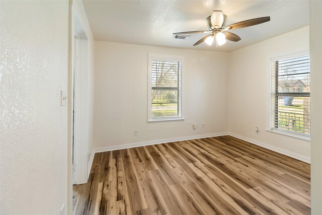 empty room featuring a wealth of natural light, visible vents, baseboards, and wood finished floors