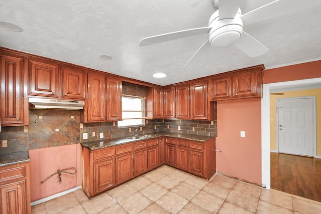 kitchen featuring under cabinet range hood, brown cabinetry, a ceiling fan, and a sink