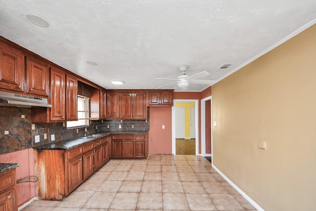 kitchen featuring baseboards, under cabinet range hood, decorative backsplash, brown cabinetry, and a ceiling fan