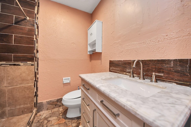 full bathroom featuring vanity, stone tile flooring, a shower stall, toilet, and a textured wall