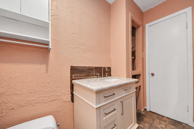 half bath with vanity, toilet, stone finish flooring, and a textured wall