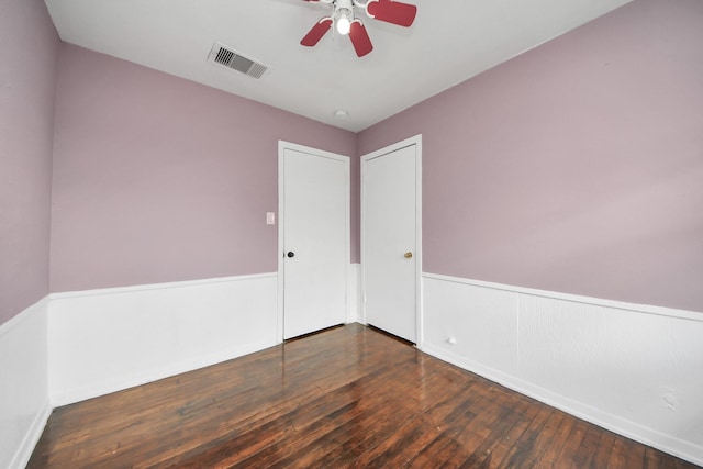 empty room with ceiling fan, visible vents, wood-type flooring, and wainscoting