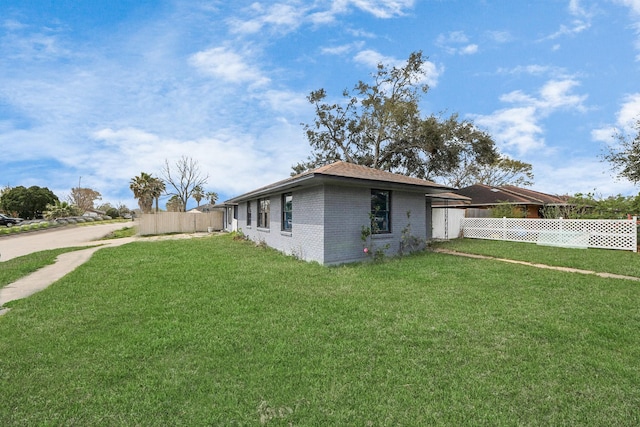 view of side of property featuring brick siding, a lawn, and fence