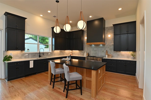 kitchen with light wood-style flooring, wall chimney exhaust hood, a center island with sink, and a sink