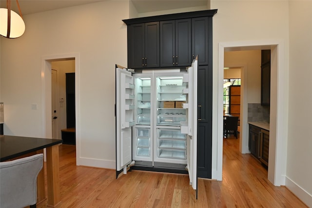 interior space with built in refrigerator, backsplash, baseboards, and light wood finished floors