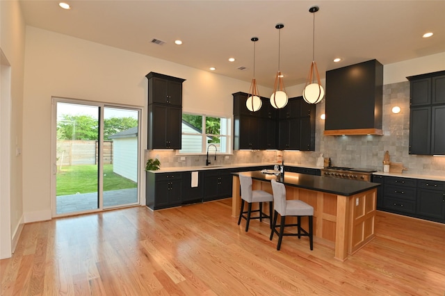 kitchen featuring tasteful backsplash, visible vents, wall chimney range hood, a center island with sink, and light wood-style floors