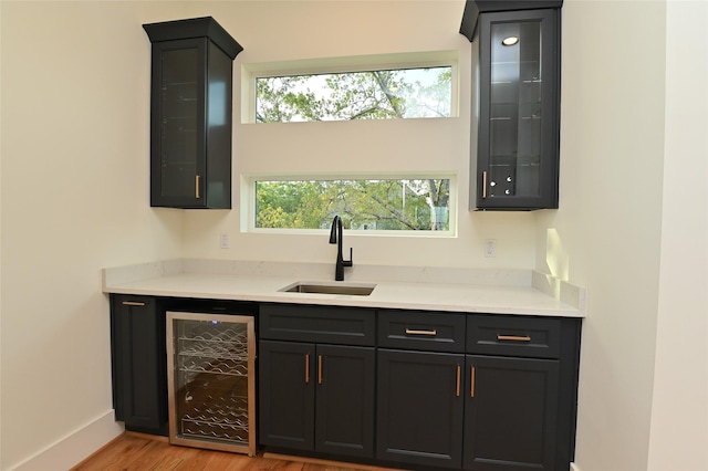 bar with beverage cooler, light wood-style flooring, baseboards, and a sink