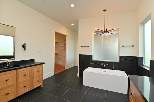 full bath with tile patterned flooring, recessed lighting, a freestanding tub, a notable chandelier, and vanity