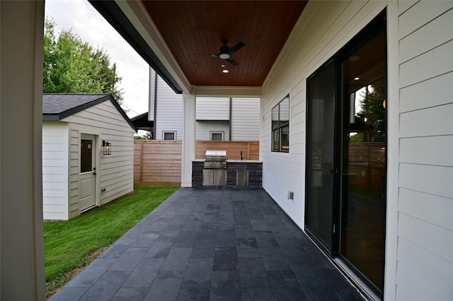 view of patio featuring an outbuilding, area for grilling, a ceiling fan, fence, and exterior kitchen