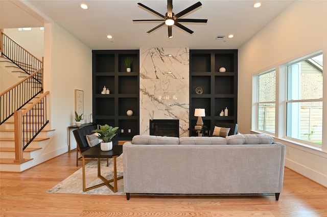 living area featuring a wealth of natural light, built in shelves, a high end fireplace, and light wood finished floors