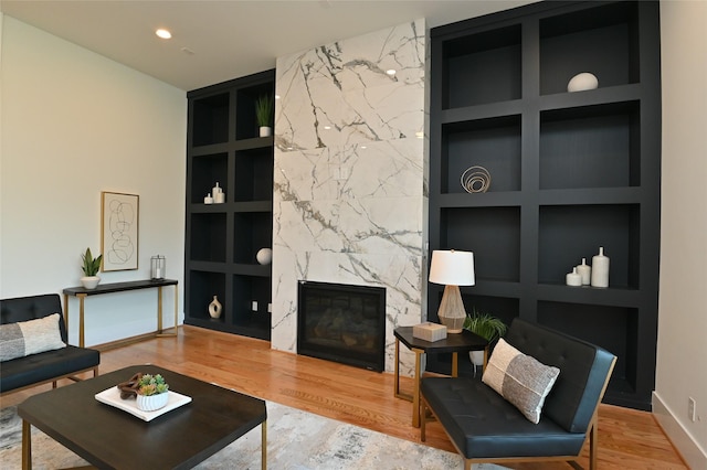 living room with built in shelves, an accent wall, wood finished floors, and a fireplace