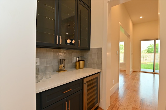 bar featuring light wood finished floors, freestanding refrigerator, a bar, wine cooler, and backsplash