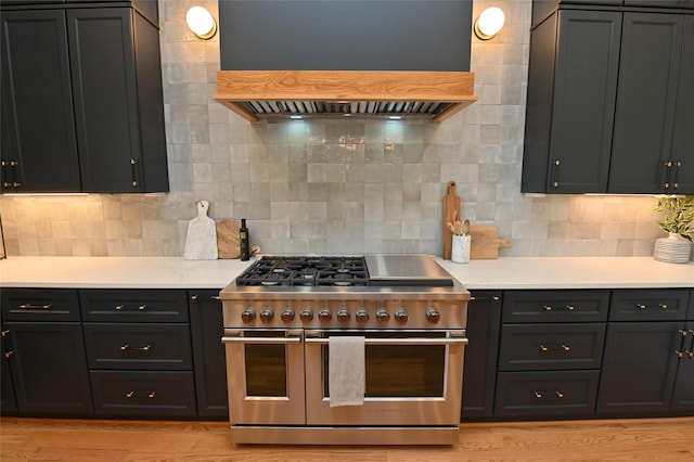 kitchen with double oven range, light countertops, decorative backsplash, light wood-style floors, and custom exhaust hood