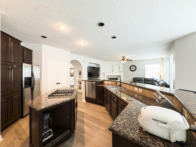 kitchen featuring a sink, a spacious island, open floor plan, stainless steel appliances, and arched walkways