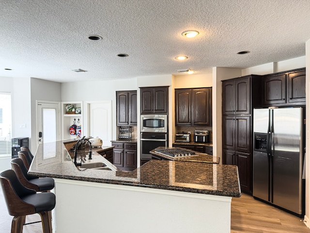 kitchen with a large island, dark brown cabinets, stainless steel appliances, and a sink