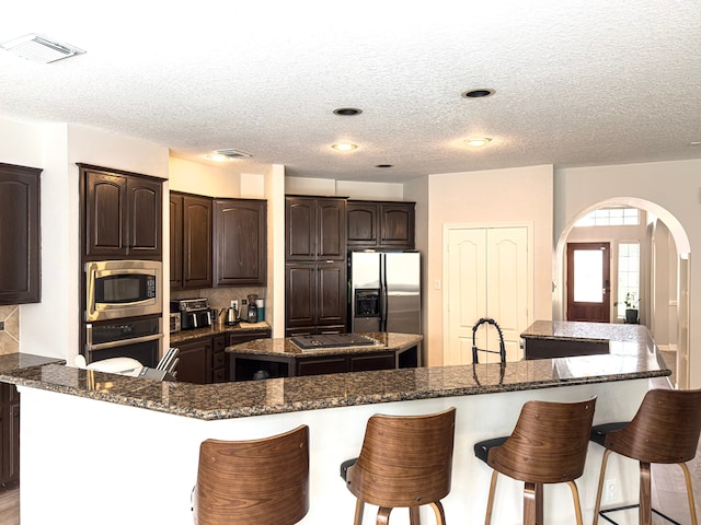 kitchen featuring visible vents, a breakfast bar, arched walkways, appliances with stainless steel finishes, and a center island