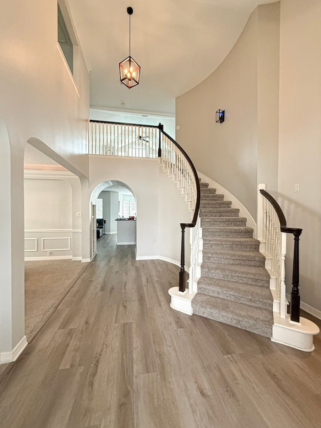 interior space featuring arched walkways, a notable chandelier, wood finished floors, and a towering ceiling