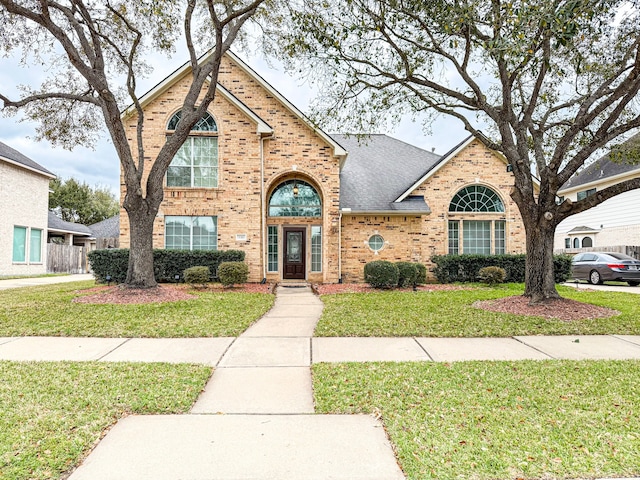 traditional-style home featuring a front lawn, brick siding, and roof with shingles