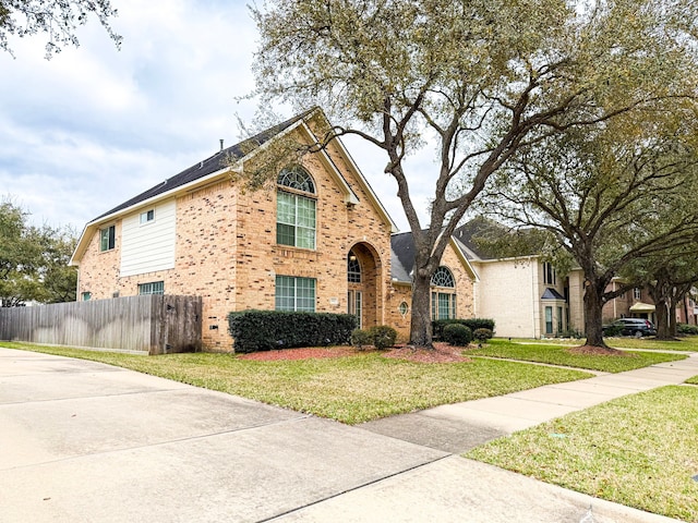 view of front of house featuring brick siding, a front lawn, and fence