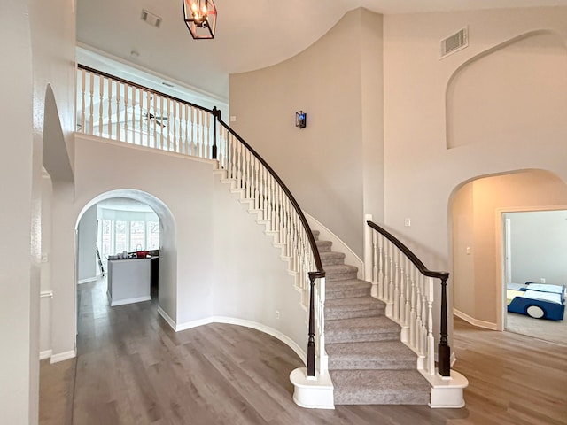 stairs with arched walkways, visible vents, and wood finished floors