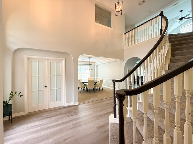 entryway featuring ceiling fan with notable chandelier, wood finished floors, arched walkways, a towering ceiling, and stairs