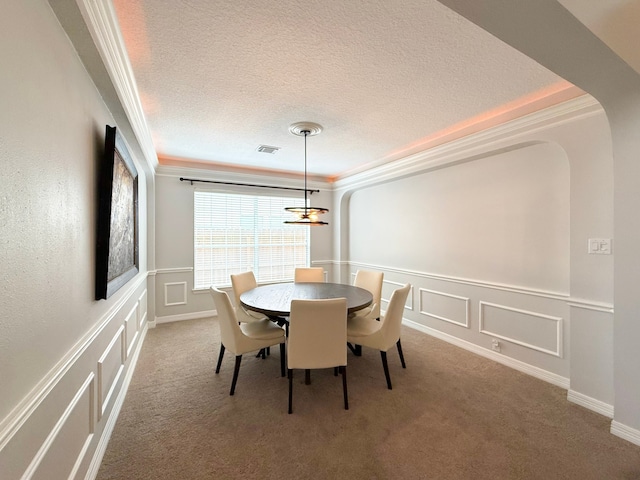 carpeted dining room with visible vents, crown molding, a wainscoted wall, a decorative wall, and a textured ceiling