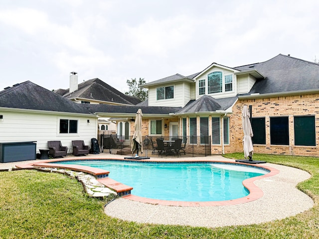 rear view of property featuring brick siding, a patio area, an outdoor pool, and a lawn