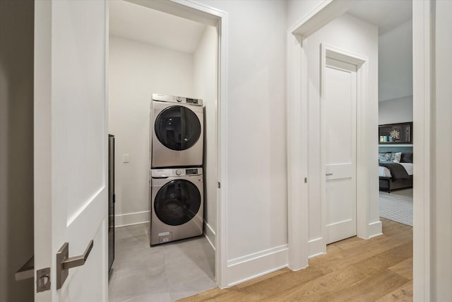 washroom with stacked washer / dryer, light wood-style flooring, laundry area, and baseboards