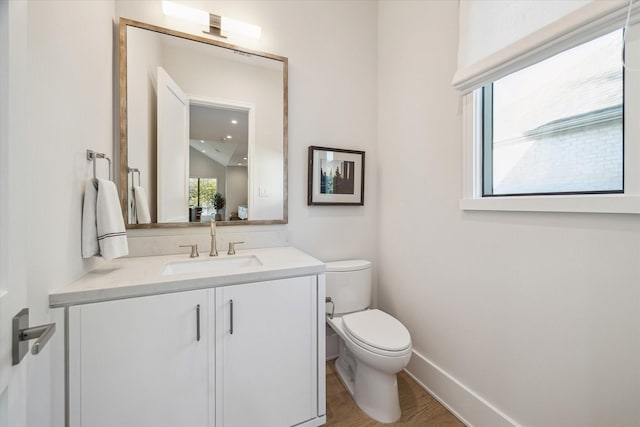 bathroom with vanity, toilet, wood finished floors, and baseboards