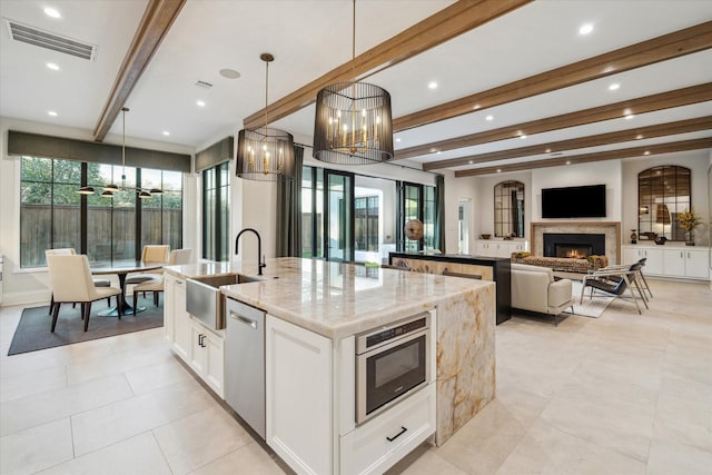 kitchen featuring visible vents, an island with sink, beam ceiling, stainless steel dishwasher, and a sink