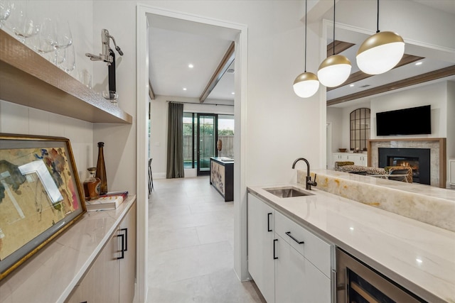 kitchen featuring beverage cooler, a sink, decorative light fixtures, open floor plan, and white cabinets