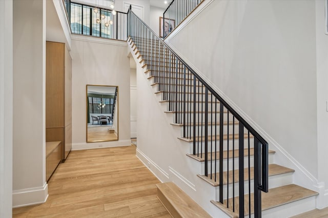 staircase featuring a high ceiling, wood finished floors, baseboards, and a chandelier