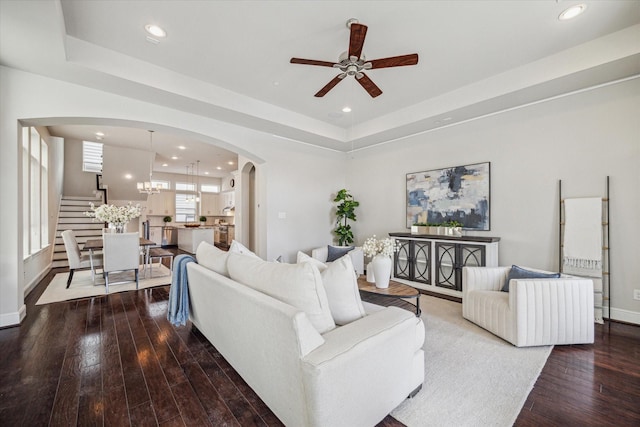 living area with a tray ceiling, hardwood / wood-style floors, recessed lighting, arched walkways, and baseboards